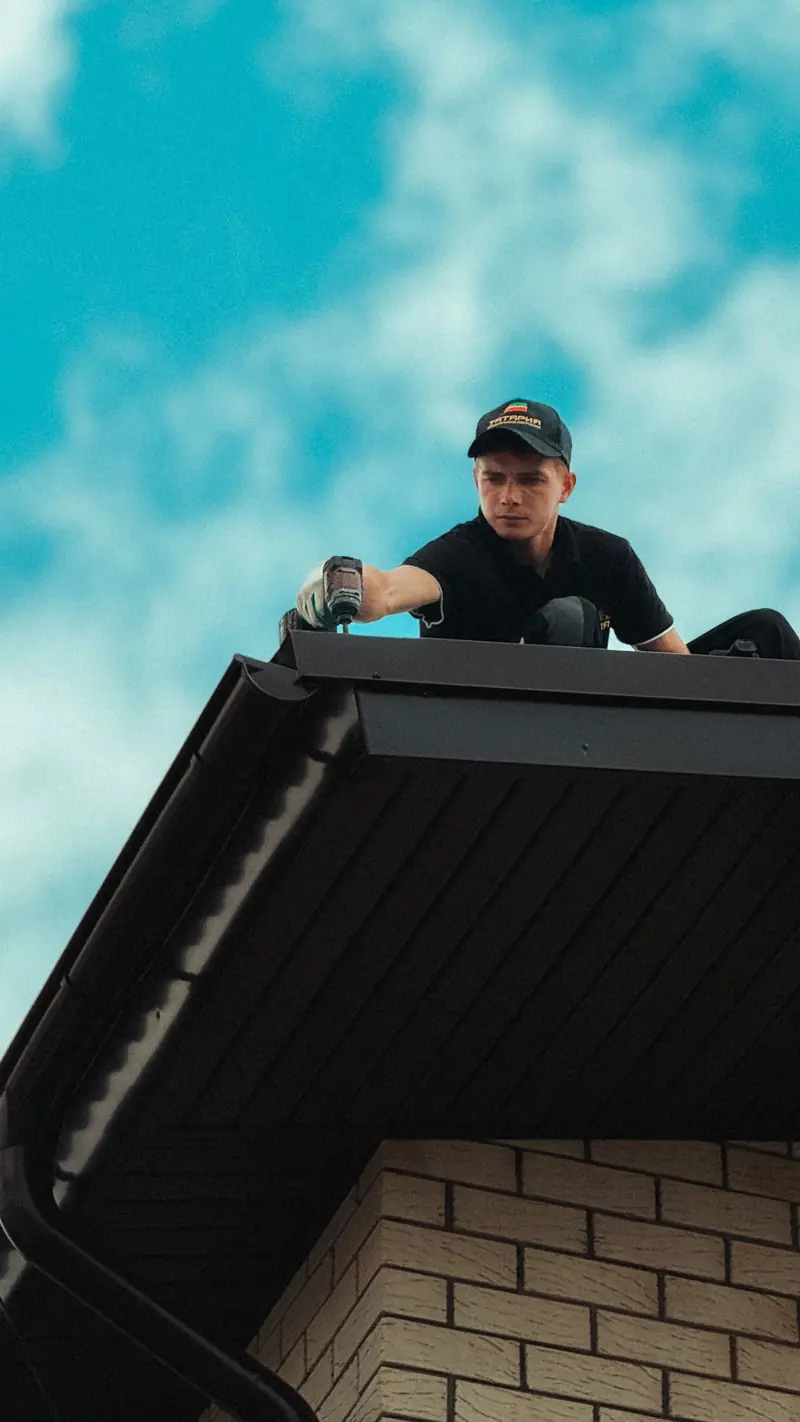 Roofer working on the edge of a house roof against a blue sky